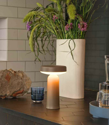 Bærbar Muuto-bordlampe på en mørk køkkenbordplade med blomsterdekoration.