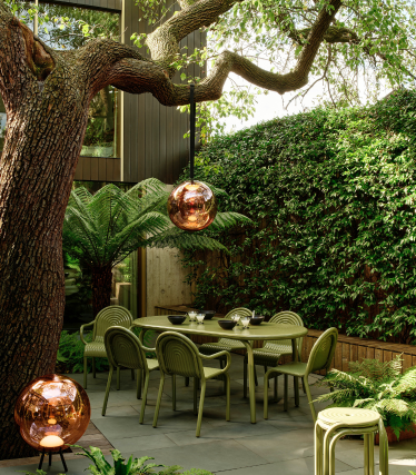 Tom Dixon-udendørslamper i en stilfuld have med spiseplads under et gammelt træ.