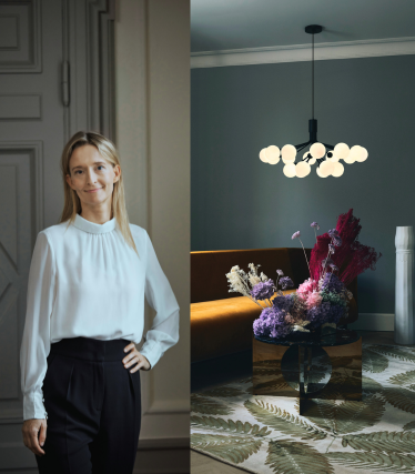 Portræt af designer Sofie Refer ved siden af en lysende pendellampe fra Nuura i et stilfuldt interiør med blomster.