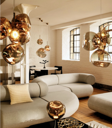 Guldfarvede Melt-pendler over en lys sofa i en loftlejlighed med sprossede vinduer.