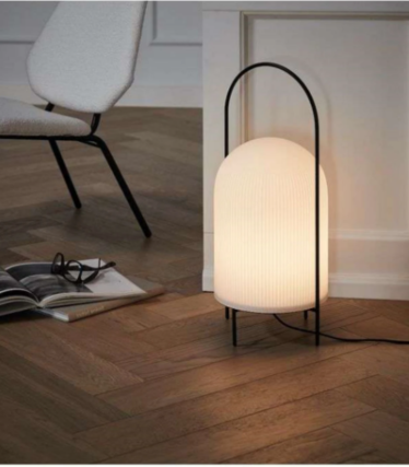 Hvid rillet lampe med sort bøjleramme på sildebensparket ved siden af en lænestol.